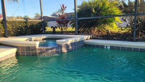 A swimming pool with a hot tub, surrounded by plants and a clear water depth marker. - New to rentals, South Facing pool and spa, free WiFi, smart TV's, 2 Master suites (Haines City)