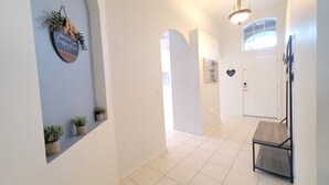 A hallway with white walls, a tiled floor, and a wooden bench. There are small potted plants on the wall and a sign that says "this is our happy place." - New to rentals, South Facing pool and spa, free WiFi, smart TV's, 2 Master suites (Haines City)