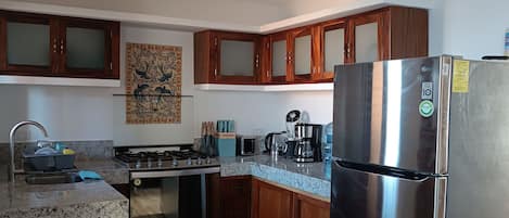 Een moderne keuken met granieten aanrechtbladen, roestvrijstalen apparatuur, houten kastjes en een gasfornuis.