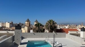 Ein Pool auf dem Dach mit freiem Blick auf die Stadtlandschaft, darunter eine Kirche mit zwei Türmen und Palmen.