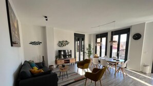 Ein modernes Wohnzimmer mit einer schwarzen Couch, einem Fernseher und einem Essbereich mit Tisch und Stühlen.