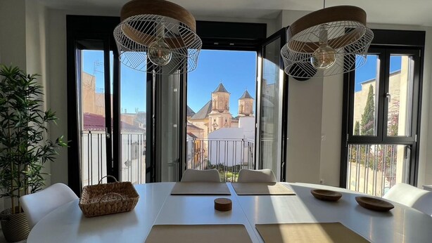 Ein moderner Essbereich mit großem Tisch, weißen Stühlen und Blick auf ein historisches Gebäude durch große Fenster.