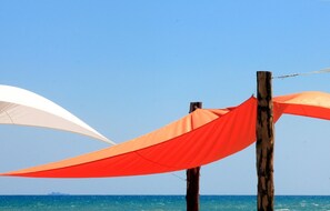 Une plage avec un poteau en bois et deux parasols, l’un blanc et l’autre orange.