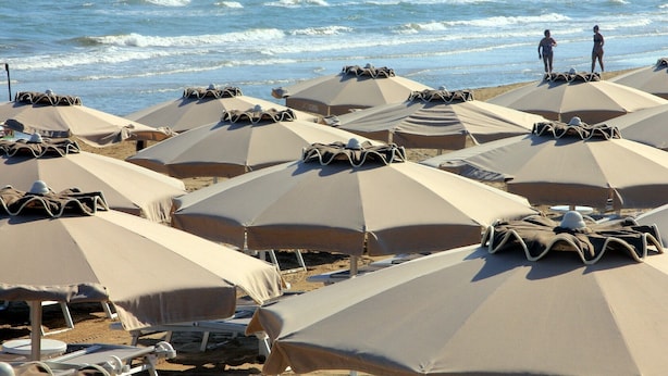 A beach with rows of sun umbrellas and lounge chairs, some occupied, others empty.