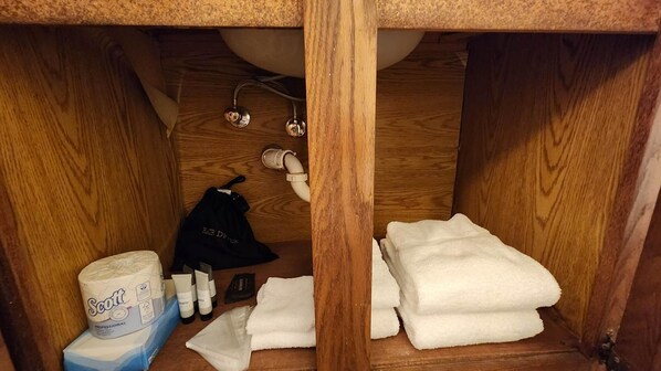 A bathroom with a wooden vanity, a towel rack, and toiletries including a Scott brand toilet paper roll.