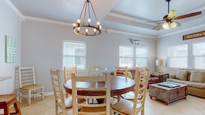 Un salón amplio con una mesa de comedor de madera rodeada de sillas, una mesa redonda de centro y un ventilador de techo.