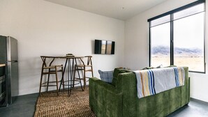 Een moderne woonkamer met een groene bank, een klein houten tafeltje en een groot raam met uitzicht op een bergachtig landschap.