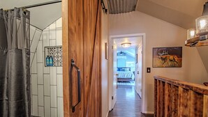 Un pasillo con puerta de madera, zona de ducha y cama al fondo.