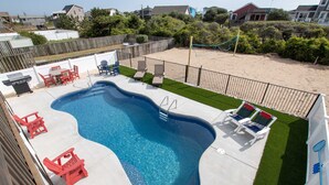 A swimming pool with a deck, red chairs, and a barbecue grill.