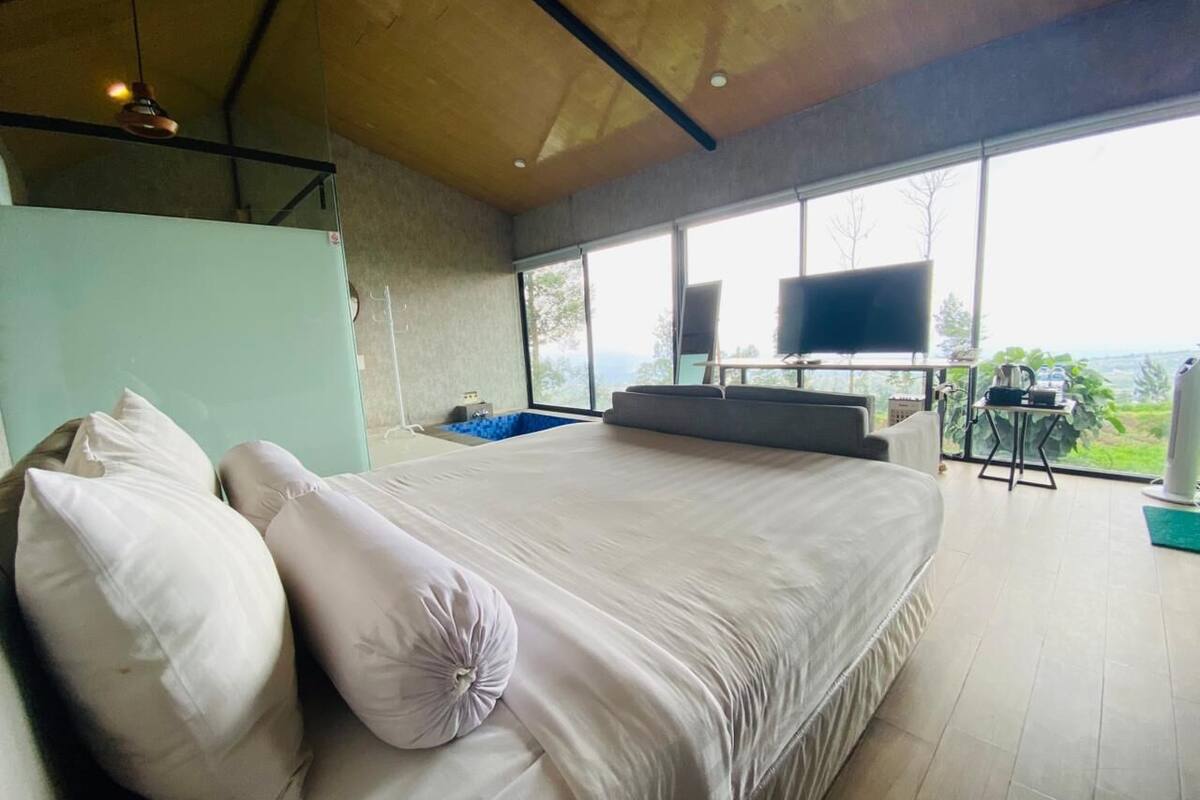 A large bed with pillows, a TV, and a view of the outdoors.
