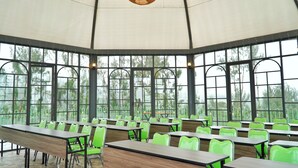 Une grande pièce ouverte, avec de longues tables et des chaises vertes, de grandes fenêtres et un plafond haut.