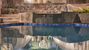 Une piscine dans laquelle se reflète un bâtiment, ainsi que des chaises.