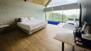 Une chambre moderne avec un grand lit, un petit bureau et une vue sur la verdure grâce à de grandes fenêtres.