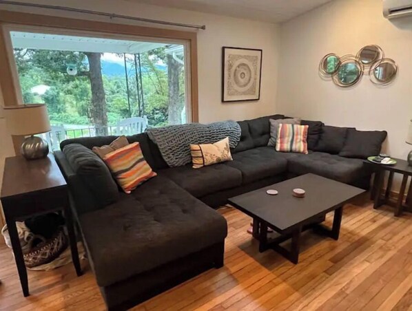 A modern living room with a sectional sofa, a coffee table, and a view of the outdoors. - Blue Ridge Mountain Cottage close to everything Asheville has to offer.  (Asheville)