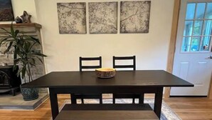 Taula de menjador amb una banca, dues cadires i tres quadres penjats a la paret.