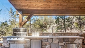 Una cocina al aire libre con pared de piedra, una parrilla y dos armarios.