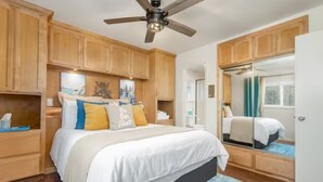 Un dormitorio con una cama, armarios de madera, un ventilador de techo y un espejo grande.