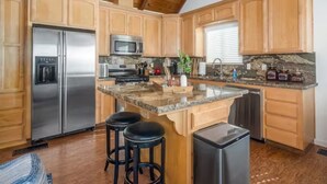Una cocina con armarios de madera, electrodomésticos de acero inoxidable, encimera de granito y una isla central con taburetes.