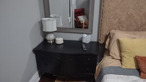Une chambre à coucher avec une commode sombre, une table de chevet avec une lampe, une télécommande et une boîte de mouchoirs.