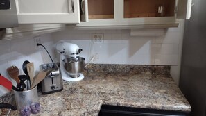 A kitchen with a granite countertop, a mixer, and various utensils.