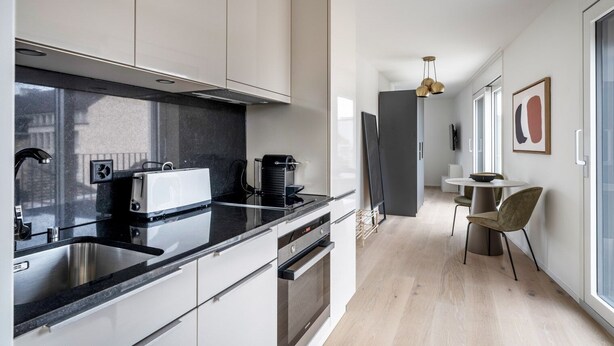 A modern kitchen with a black countertop, stainless steel appliances, and a dining area with a round table and chairs.
