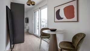A modern living room with a minimalist design, featuring a round table, two chairs, a flat-screen TV, and a large abstract painting.
