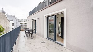 A modern building with a balcony, a sliding glass door, and a small outdoor seating area.