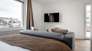 A modern hotel room with a large bed, a flat-screen TV, and a city view.