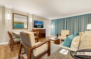 A hotel room with a dining area, a sofa set, a television, and a view of the outdoors.