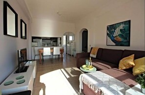 Un soggiorno moderno con un divano, un'area pranzo con sedie e una cucina sullo sfondo.