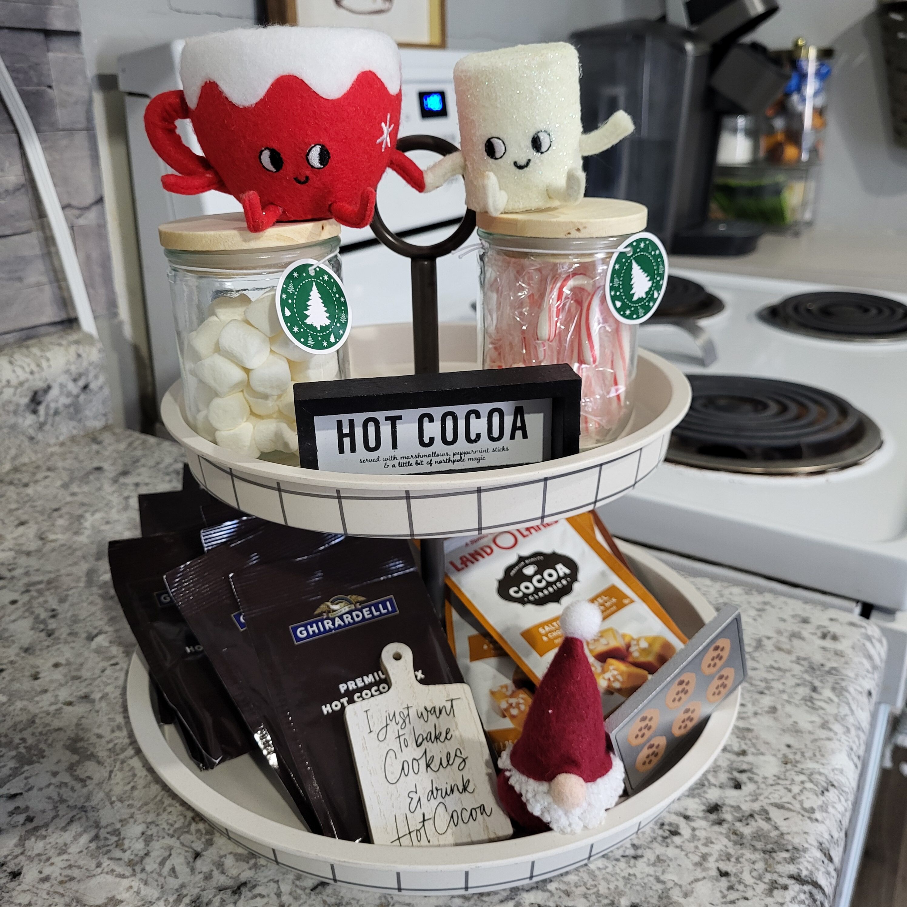 En bordplade i et køkken med udstilling af ingredienser til varm kakao, samt et skilt med teksten 'HOT COCOA'.