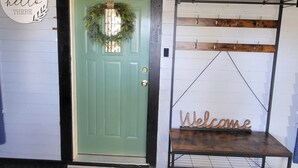 A green door with a wreath, a 'hello there' sign, a 'bright' sign, and a 'welcome' sign above a rack. - Cozy Little Getaway, Winner, SD (Winner)