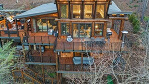 A multi-level wooden cabin with a deck, large windows, and outdoor seating areas. - Top 10 VRBO in U.S. Riverfront, Hot Tub, Sleeps 12, As seen on TV! (Epworth)