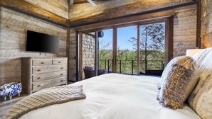 A bedroom with a large bed, a dresser, a flat-screen TV, and a balcony with a view of trees. - Top 10 VRBO in U.S. Riverfront, Hot Tub, Sleeps 12, As seen on TV! (Epworth)