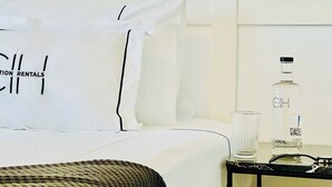 A hotel room with a neatly made bed, a bedside table with a bottle of local liquor, and a glass. - CIH Apartments (Puerta del Carmen)