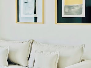 Una habitación con un sofá blanco y dos cuadros abstractos enmarcados en la pared.