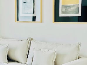 Um sofá branco com várias almofadas em um quarto com quadros abstratos na parede.