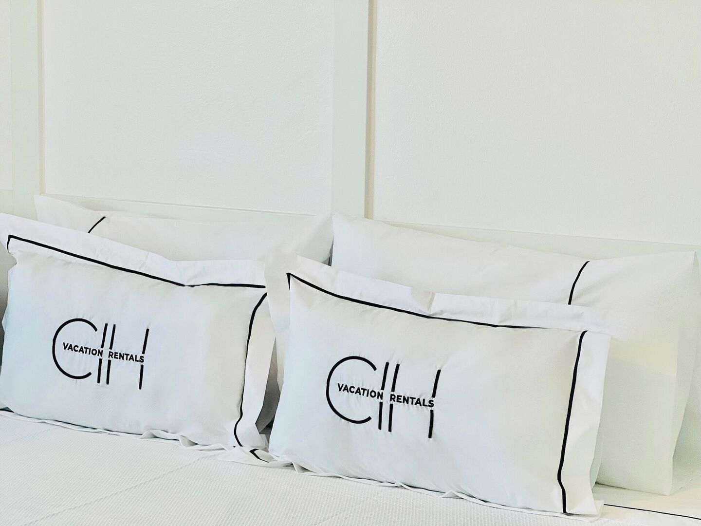 Cama com roupa de cama e almofadas brancas com a inscrição "Vacation Rentals".