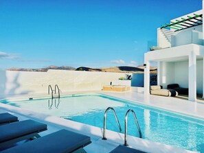 A modern pool area with clear blue water, lounge chairs, and a view of distant hills. - CIH Apartments (Puerto del Carmen)