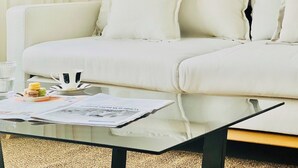 A white sofa with pillows, a glass coffee table with a magazine, a cup, and a plate of macarons. - CIH Apartments (Puerta del Carmen)