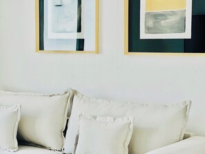 Une pièce avec un canapé blanc et deux tableaux abstraits encadrés accrochés au mur.