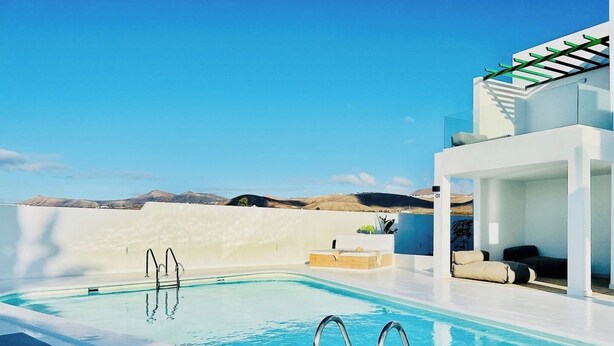 A modern pool area with clear blue water, lounge chairs, and a view of distant hills. - CIH Apartments (Puerta del Carmen)
