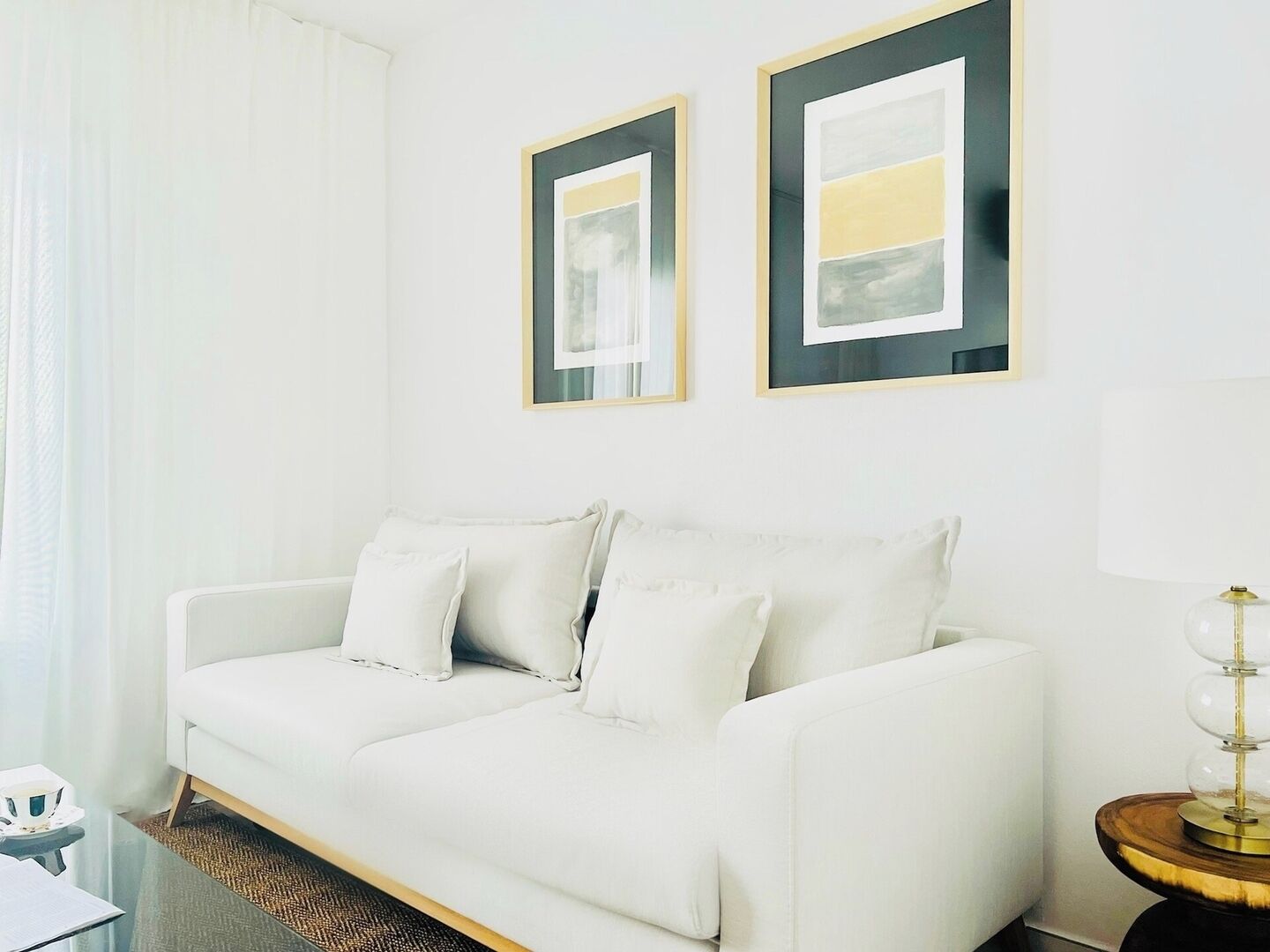 A white sofa with cushions, a glass coffee table, and a lamp on a wooden side table.