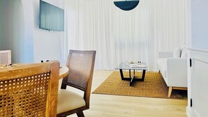 A modern living room with a round wooden table, a wicker chair, a white sofa, and a television mounted on the wall. - CIH Apartments (Puerta del Carmen)