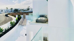 Un edificio moderno y blanco con un balcón de vidrio que da a una carretera y un cielo despejado.