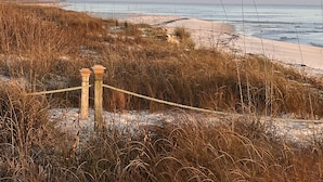 Een strand met een houten omheining en touwbordes, zandduinen en een heldere lucht.