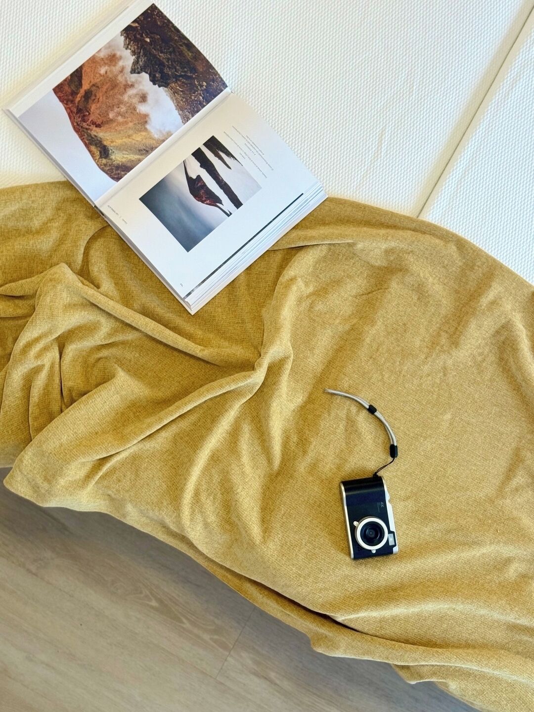 A room with a yellow fabric spread on the floor, a camera, and a magazine with photos.