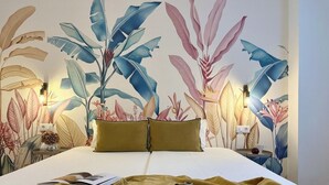 Un dormitorio con una cama grande, una mesita de noche, una lámpara y un mural de plantas tropicales en la pared.