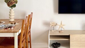 Un comedor con una mesa de madera, sillas, un jarrón con flores, un televisor de pantalla plana y un mueble de madera con objetos decorativos.