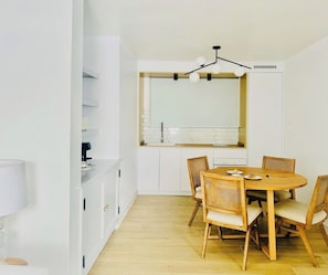 A modern kitchen with white cabinets, a wooden dining table with six chairs, and a pendant light above the counter.